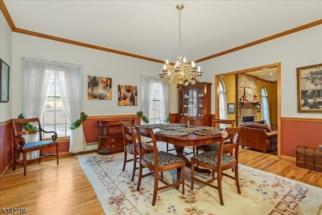 dining area featuring a brick fireplace, crown molding, light wood-style floors, and an inviting chandelier