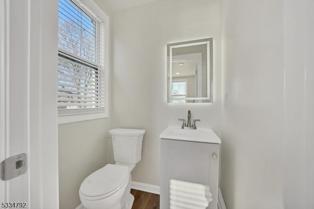 half bathroom with baseboards, vanity, toilet, and wood finished floors