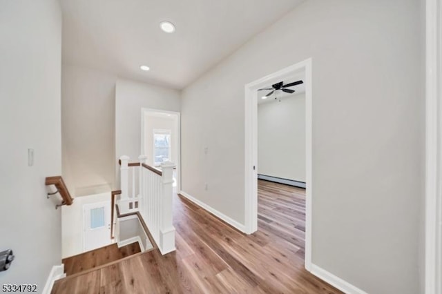 corridor featuring baseboards, a baseboard radiator, wood finished floors, an upstairs landing, and recessed lighting