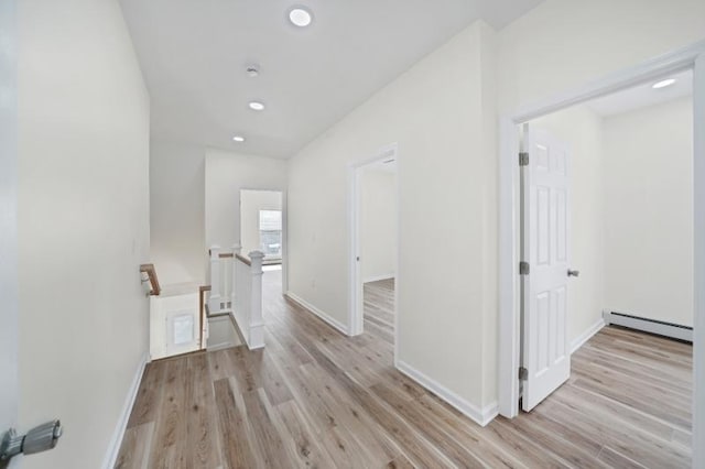 corridor featuring baseboards, baseboard heating, an upstairs landing, and light wood-style floors