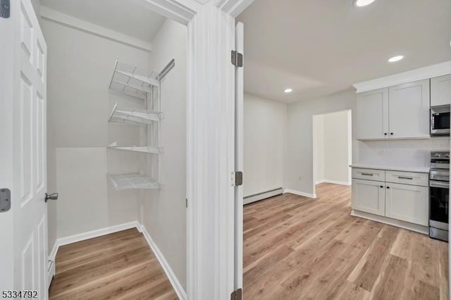 kitchen featuring appliances with stainless steel finishes, light countertops, a baseboard heating unit, and light wood-style flooring