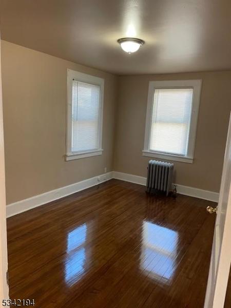 spare room featuring baseboards, radiator, and wood finished floors