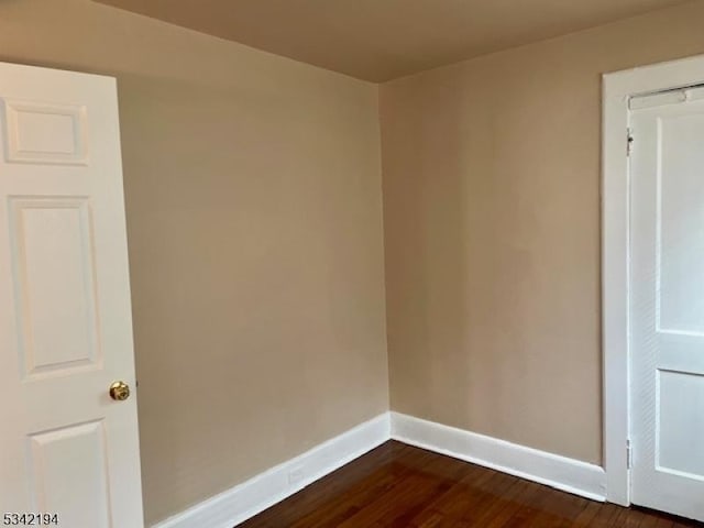 empty room featuring baseboards and dark wood-type flooring