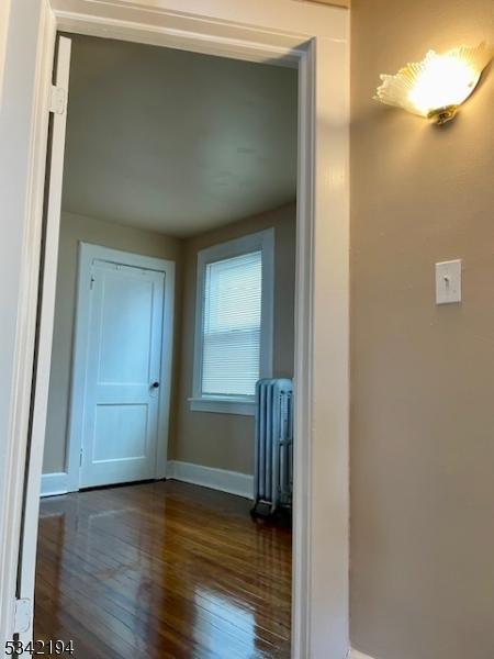 hall with radiator, baseboards, and dark wood-style flooring