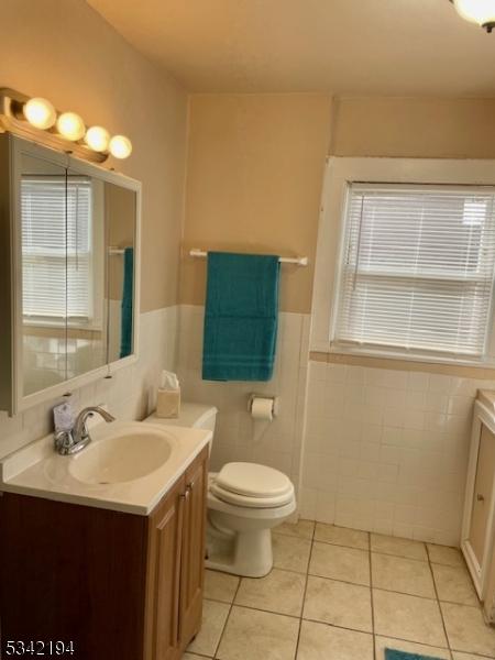 full bathroom with vanity, a wainscoted wall, tile patterned flooring, tile walls, and toilet