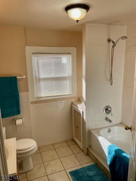 bathroom with tile patterned floors, toilet, shower / bathtub combination, tile walls, and vanity