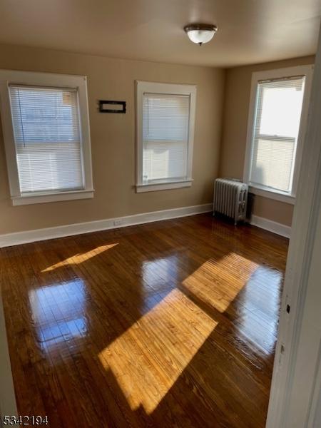 empty room with hardwood / wood-style floors, radiator heating unit, and baseboards