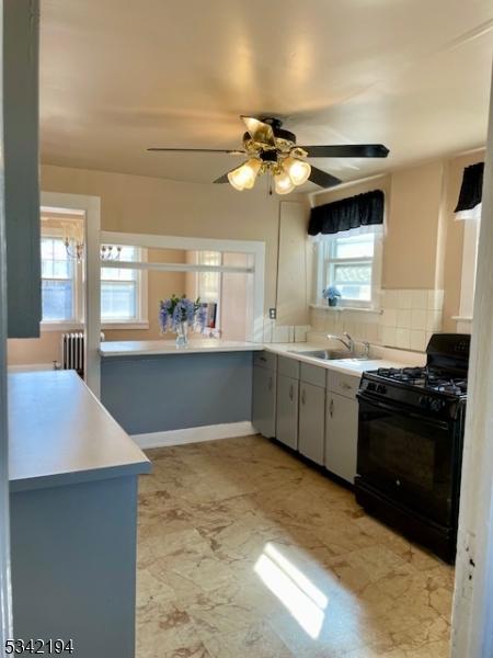 kitchen featuring a ceiling fan, black gas stove, radiator, light countertops, and decorative backsplash