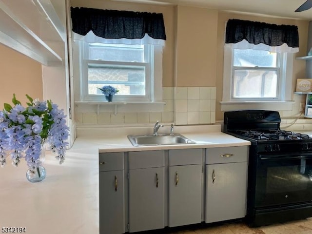 kitchen with gas stove, gray cabinets, a sink, light countertops, and tasteful backsplash