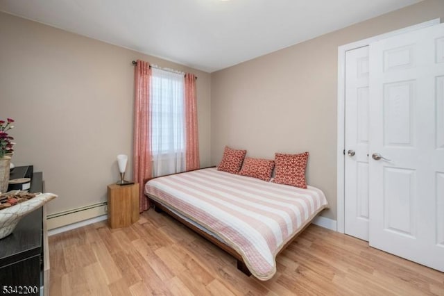 bedroom with a baseboard heating unit and light wood-style flooring