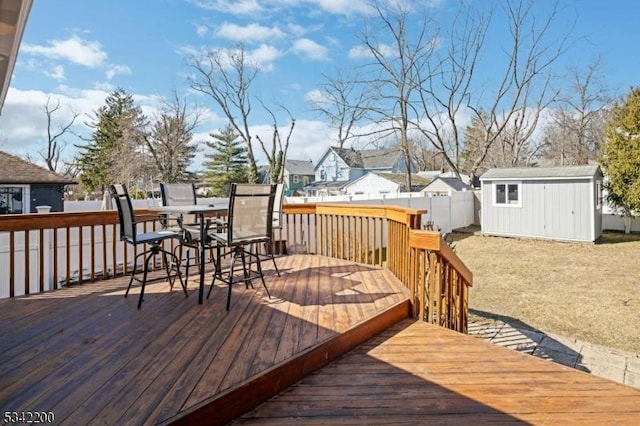 wooden deck featuring outdoor dining area, an outdoor structure, fence, a residential view, and a storage unit