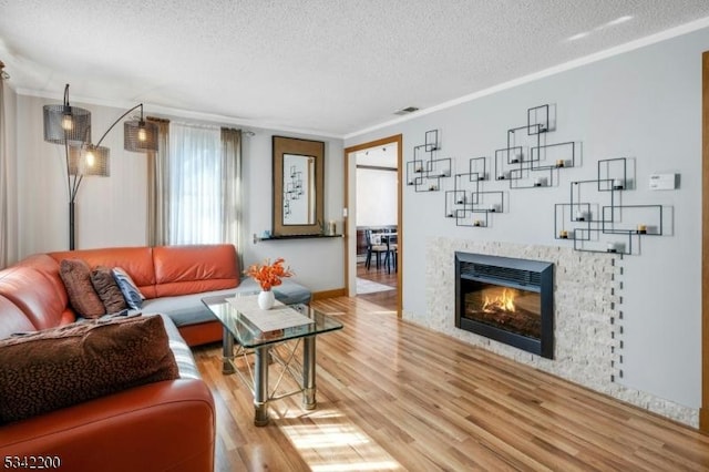 living area featuring ornamental molding, light wood-type flooring, a glass covered fireplace, and a textured ceiling