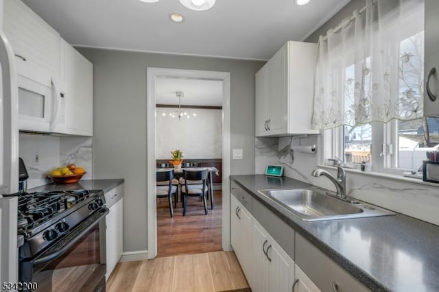 kitchen featuring black range with gas cooktop, dark countertops, light wood-style flooring, white cabinetry, and a sink