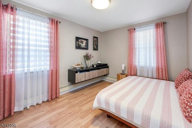 bedroom with a baseboard radiator, multiple windows, baseboard heating, and wood finished floors