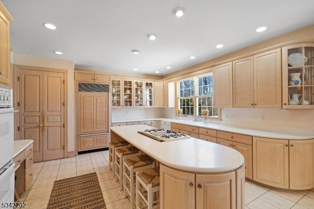 kitchen with light tile patterned floors, light brown cabinets, white appliances, a kitchen island, and light countertops