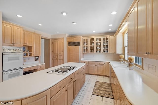 kitchen with light brown cabinetry, white appliances, a kitchen island, and a sink