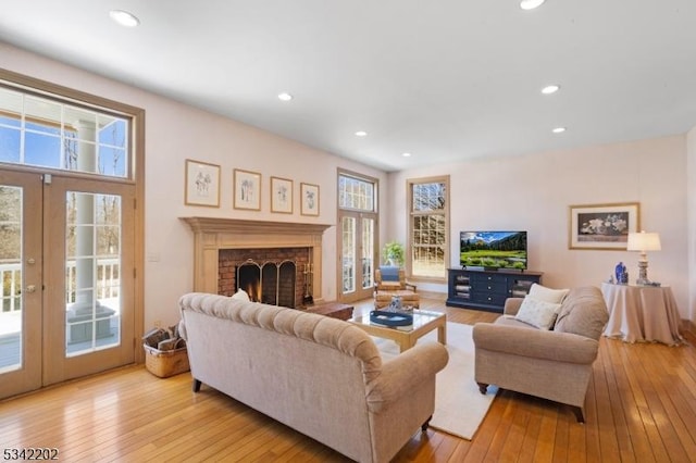 living area featuring light wood-style floors, recessed lighting, a brick fireplace, and french doors