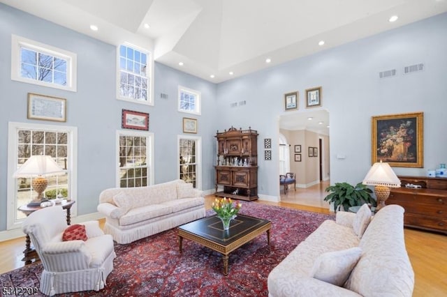 living room featuring a high ceiling, light wood-type flooring, and visible vents