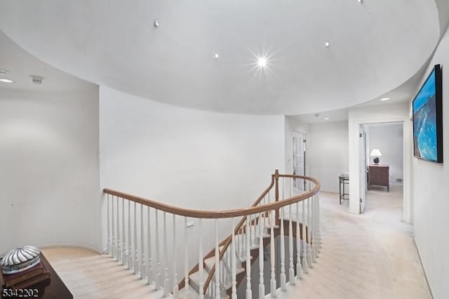 hall with wood finished floors and an upstairs landing