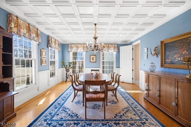 dining area with an ornate ceiling, a wainscoted wall, light wood finished floors, and an inviting chandelier