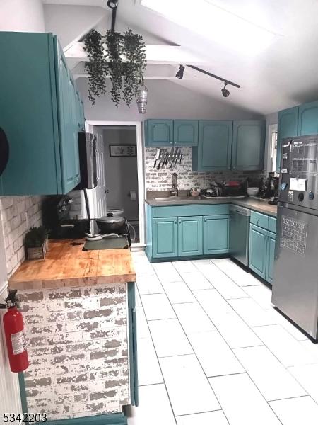 kitchen with blue cabinetry, lofted ceiling, decorative backsplash, stainless steel dishwasher, and a sink