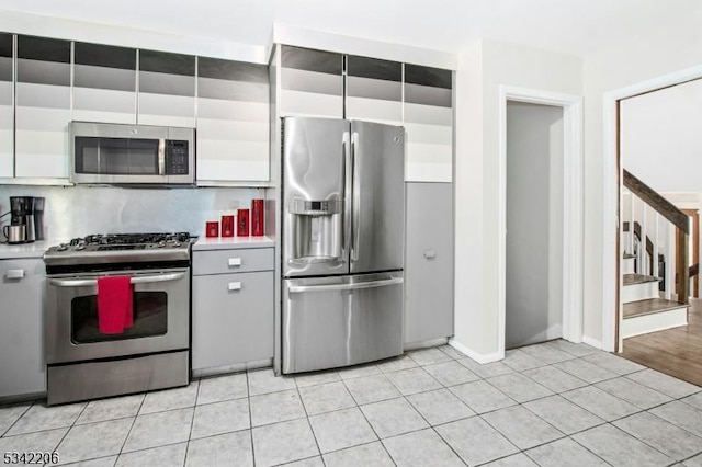 kitchen featuring light tile patterned floors, white cabinets, light countertops, appliances with stainless steel finishes, and decorative backsplash