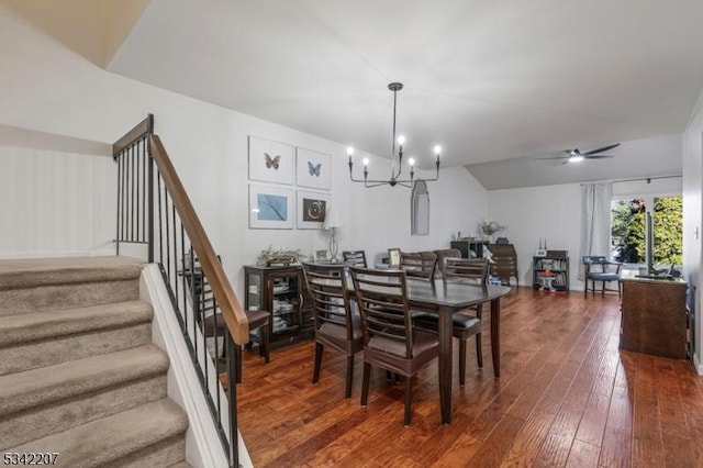 dining area with ceiling fan with notable chandelier, stairs, lofted ceiling, and dark wood-style flooring