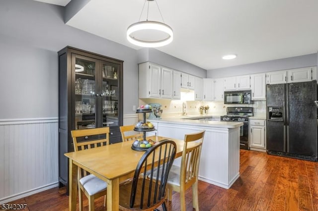 kitchen featuring dark wood finished floors, wainscoting, black appliances, and light countertops