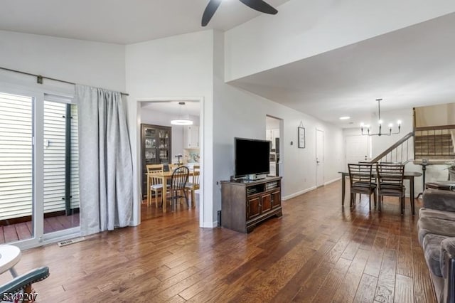 living area featuring baseboards, dark wood-style flooring, and ceiling fan with notable chandelier