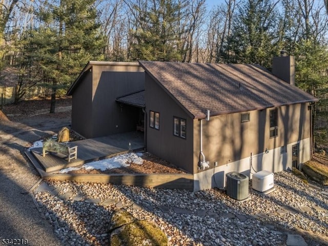 view of property exterior featuring central AC, a chimney, and a shingled roof