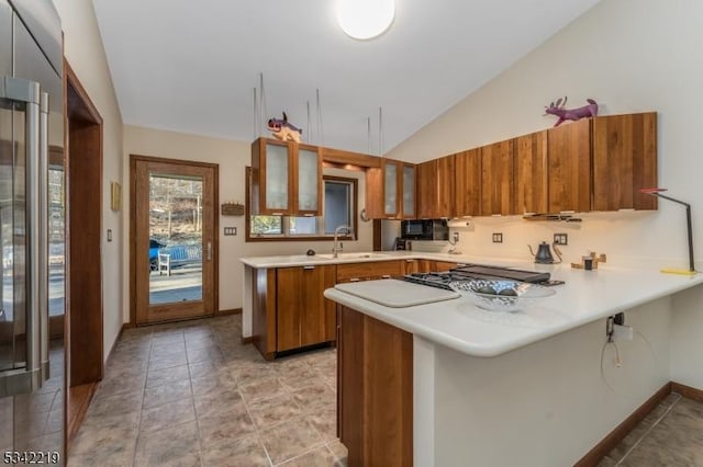 kitchen with a sink, a peninsula, brown cabinetry, glass insert cabinets, and lofted ceiling