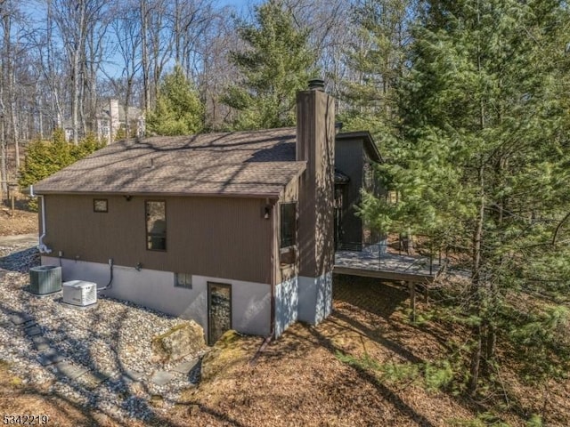 view of property exterior featuring a wooden deck, a chimney, and a shingled roof