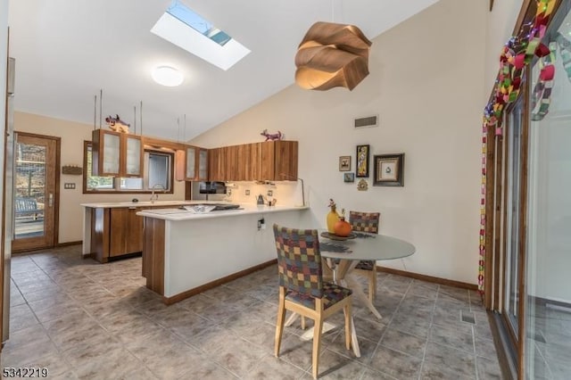 kitchen with glass insert cabinets, light countertops, brown cabinets, a peninsula, and a skylight