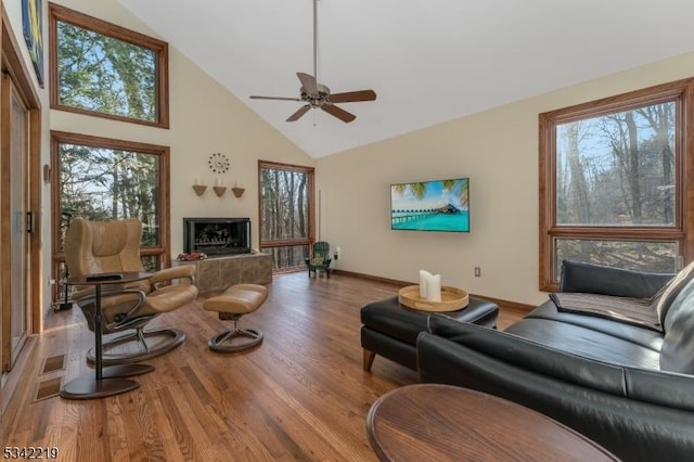 living room with a fireplace with raised hearth, a healthy amount of sunlight, high vaulted ceiling, and wood finished floors