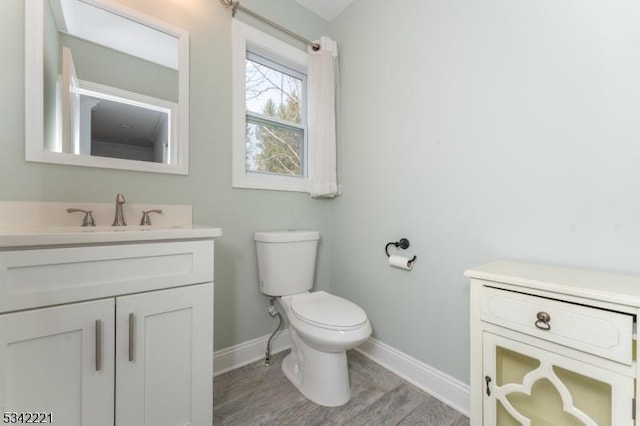 half bathroom with toilet, baseboards, wood finished floors, and vanity