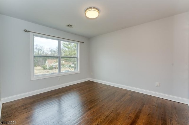 spare room featuring visible vents, baseboards, and dark wood-type flooring