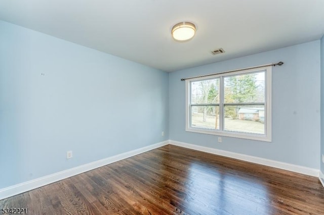 unfurnished room with dark wood-type flooring, visible vents, and baseboards