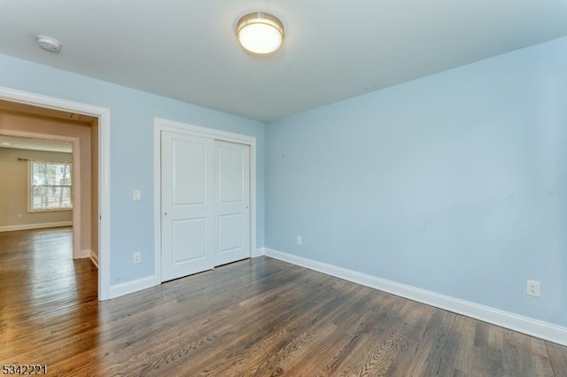 unfurnished bedroom featuring a closet, baseboards, and dark wood-style flooring