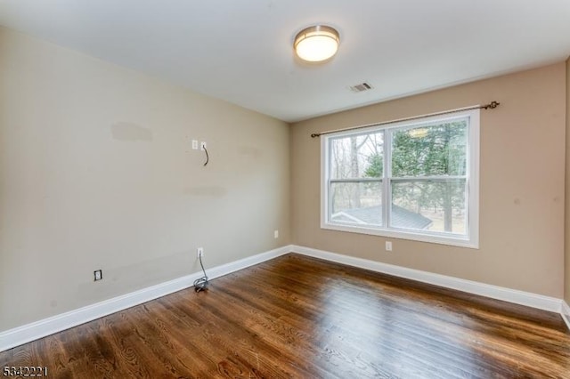 unfurnished room featuring dark wood-style floors, visible vents, and baseboards