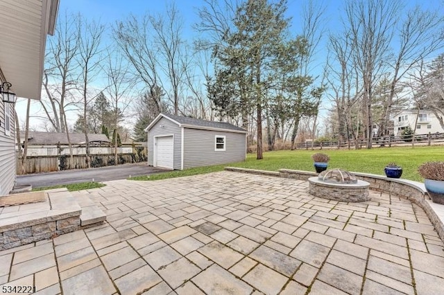 view of patio with an outdoor fire pit, aphalt driveway, a garage, an outdoor structure, and fence