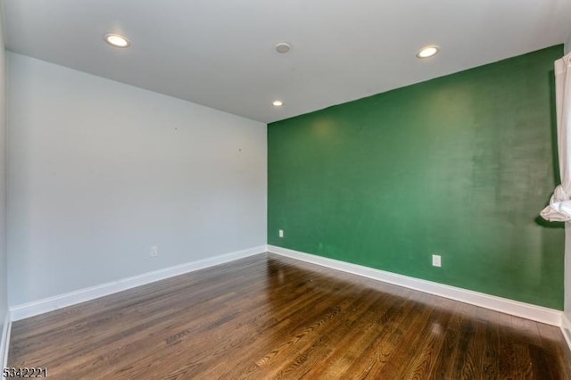 spare room with an accent wall, recessed lighting, baseboards, and wood finished floors