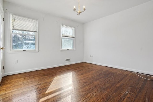 unfurnished room with visible vents, wood finished floors, baseboards, and a chandelier