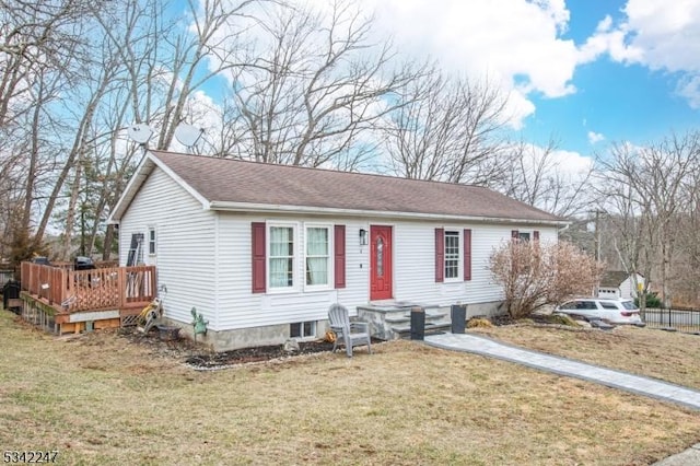 view of front of home featuring roof with shingles, a wooden deck, and a front yard