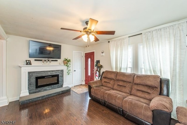 living room featuring ceiling fan, baseboards, wood finished floors, and a stone fireplace