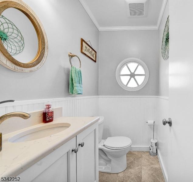 half bathroom featuring a wainscoted wall, visible vents, crown molding, and toilet