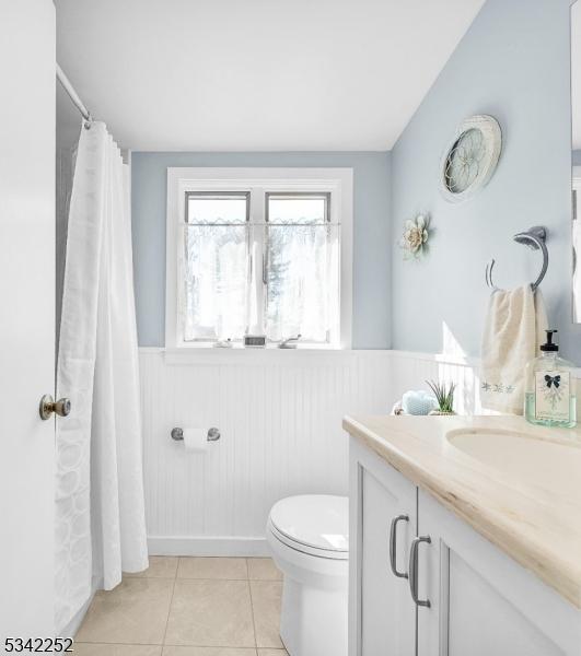 full bath with curtained shower, toilet, a wainscoted wall, vanity, and tile patterned floors