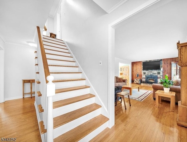 staircase with a stone fireplace, ornamental molding, wood finished floors, and baseboards