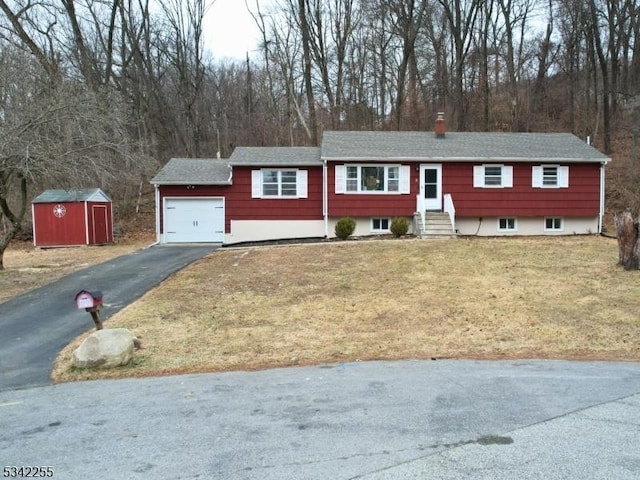 ranch-style house with a chimney, aphalt driveway, an attached garage, a storage unit, and a front lawn