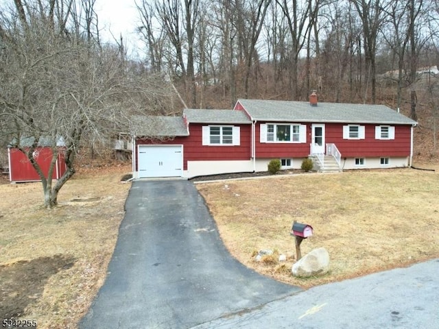 view of front facade featuring aphalt driveway, a front yard, a chimney, and an attached garage