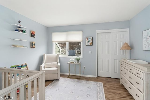 bedroom with a crib, a closet, wood finished floors, and baseboards